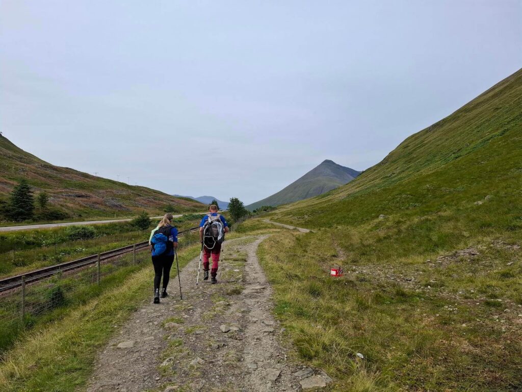Two hikers walking beside railway tracks towards Ben Dorain
