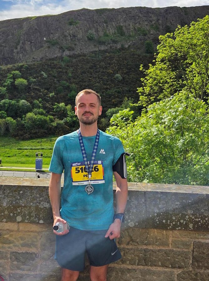 Peter Whyte with his medal after the Edinburgh Marathon Festival 10K, Salisbury Crags behind