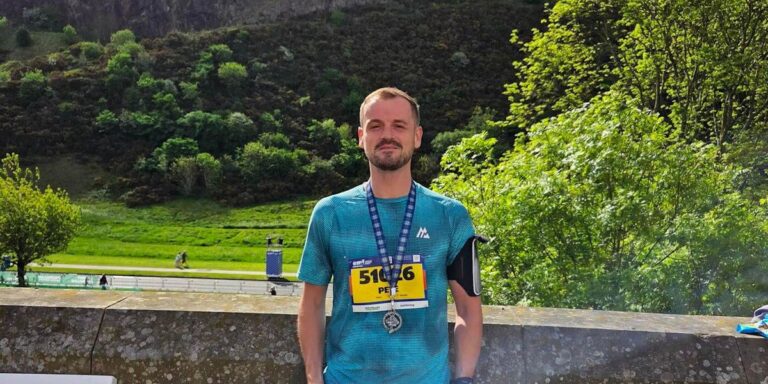 Peter Whyte with his race number and medal after the Edinburgh Marathon Festival 10K, Salisbury Crags behind